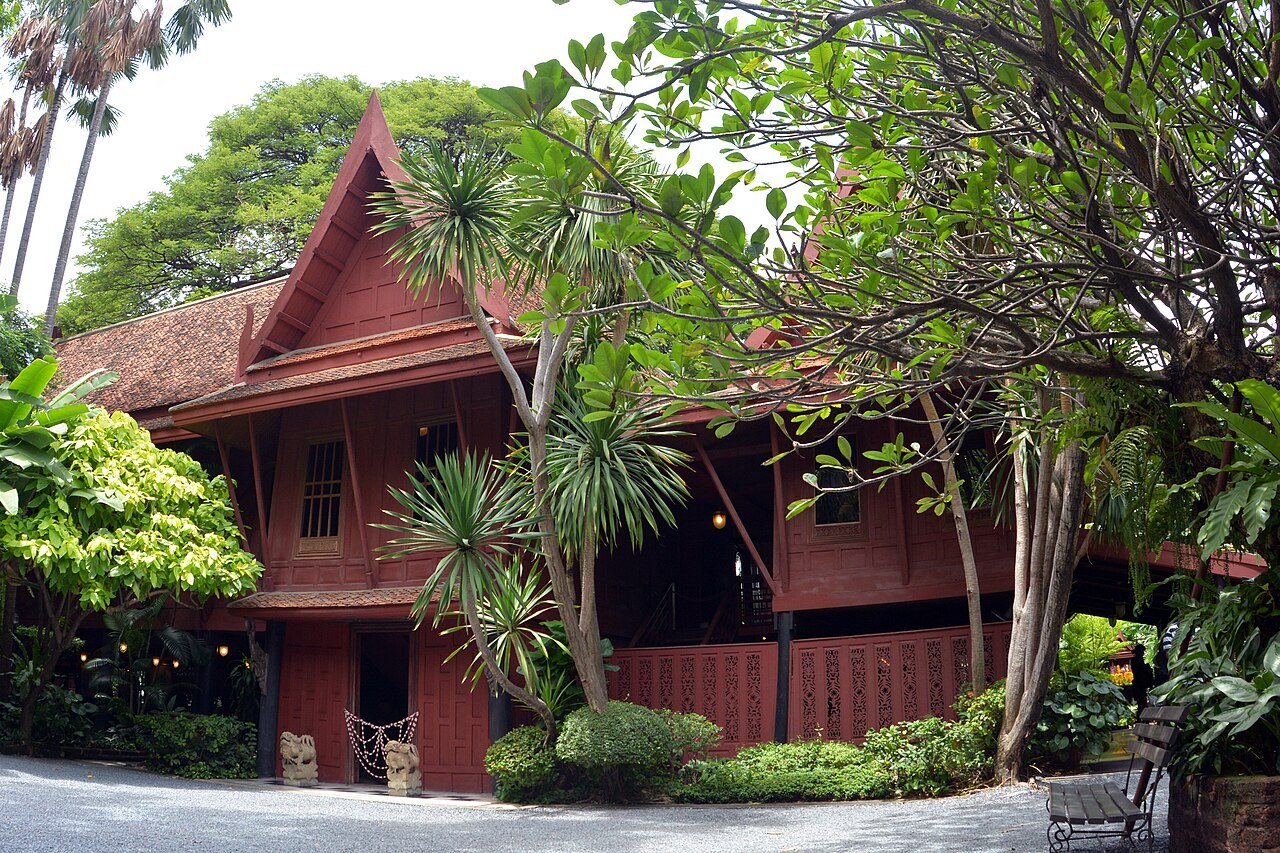 The main wooden house at Jim Thompson House surrounded by trees and a garden