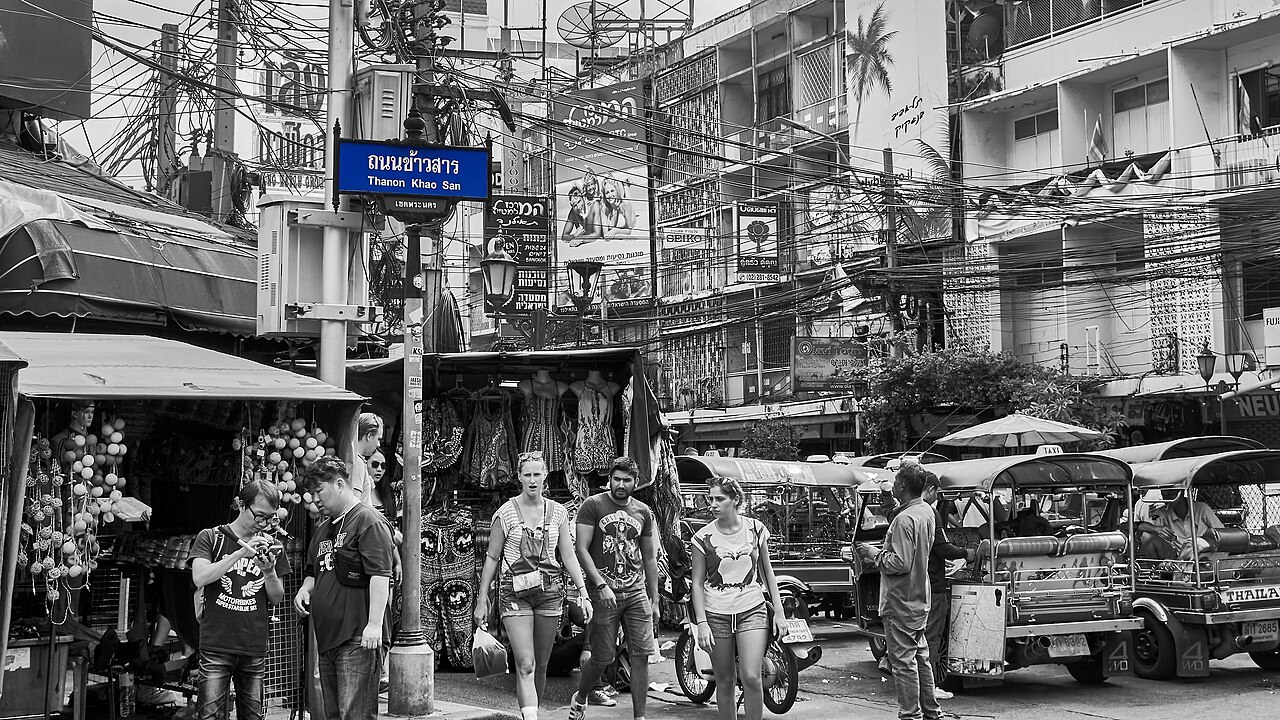 Shops and a tuk-tuk beneath a blue Khao San Road street sign